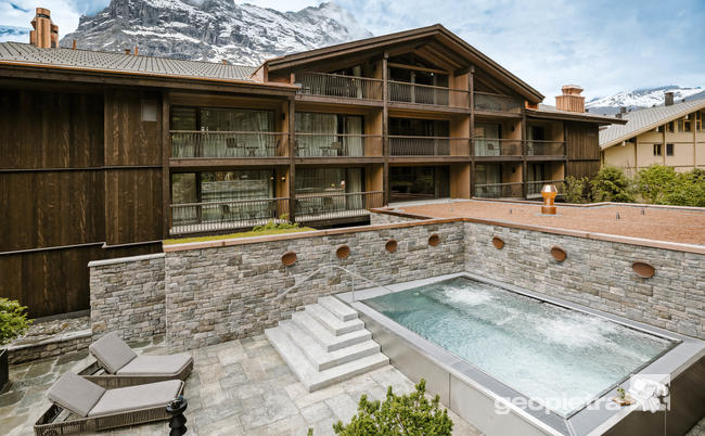 Mountain hotel with a pool and manufactured stone wall cladding by Geopietra, overlooking snowy mountains.